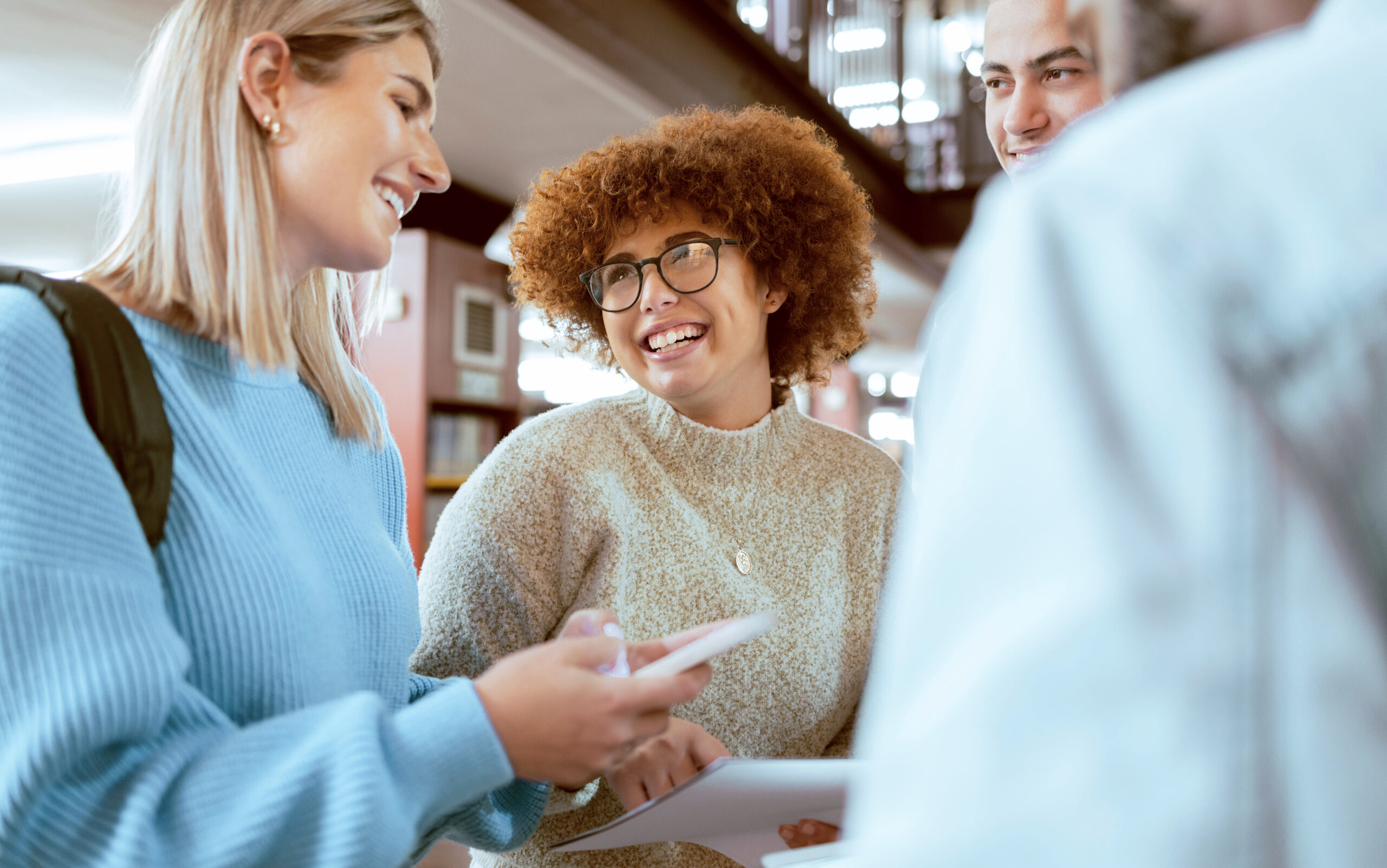 Happy, education or students with phone in library for research, collaboration or project management. Smile, documents or university people group on tech for learning, scholarship study or web search.